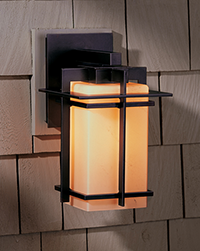 A Hubbardton Forge Tourou Outdoor Wall Light lit against a house.