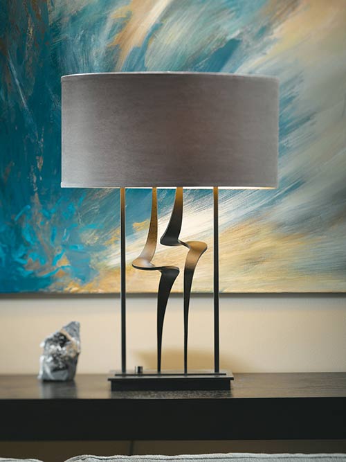 This Hubbardton Forge light is a beautiful table lamp set against a blue painting | Capitol Lighting