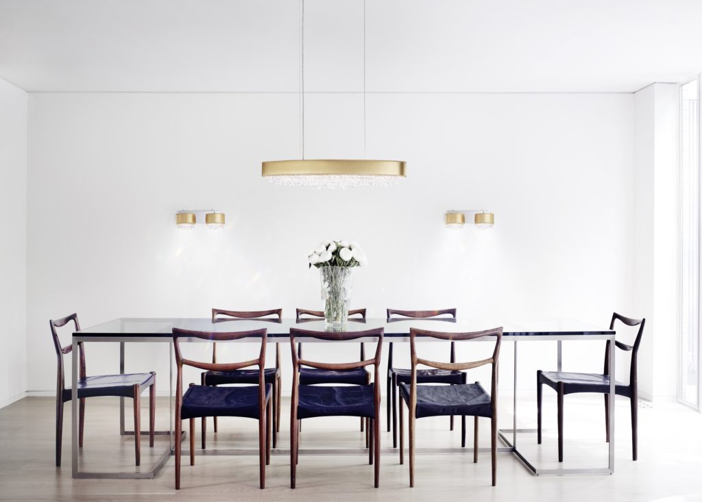 An elongated gold pendant light with crystal accents hangs in the middle of a minimal-frills contemporary dining room