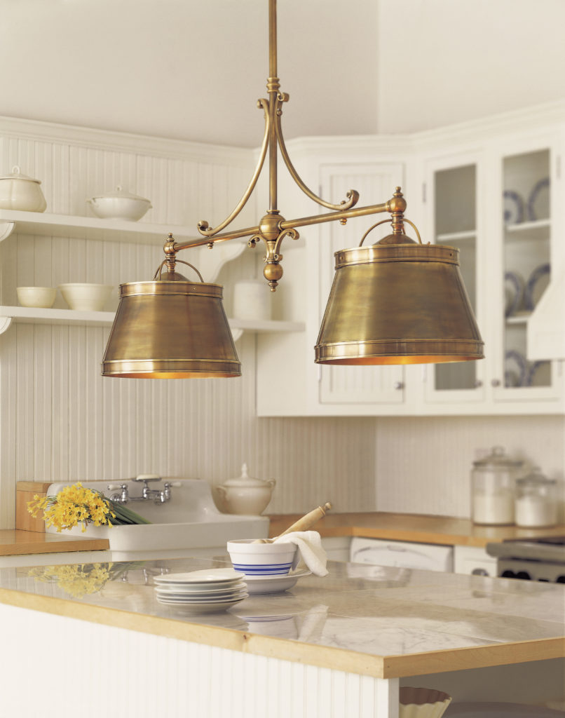 An antique brass linear pendant with two cone shades sends warm glow over a farmhouse kitchen island