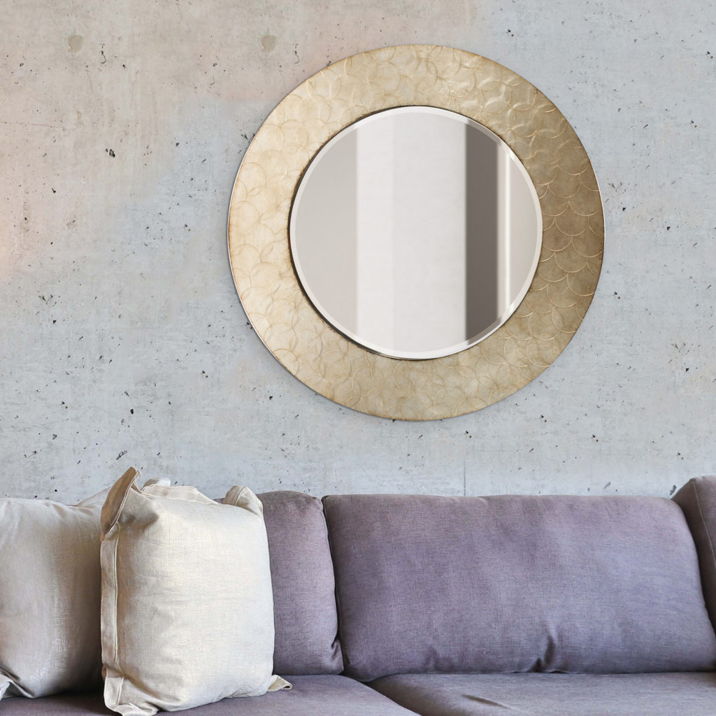 Round Camelot Wall Mirror Hangs on textured living room wall above purple sectional sofa
