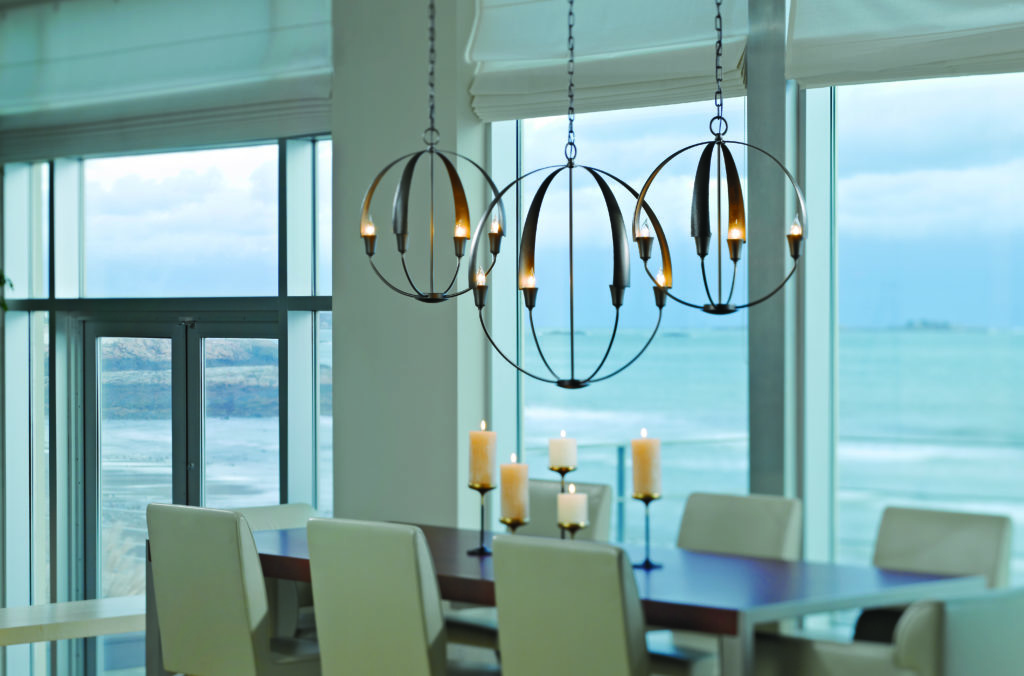 3 Wrought Iron Cirque Chandeliers hang over a long dining room table in a waterfront home