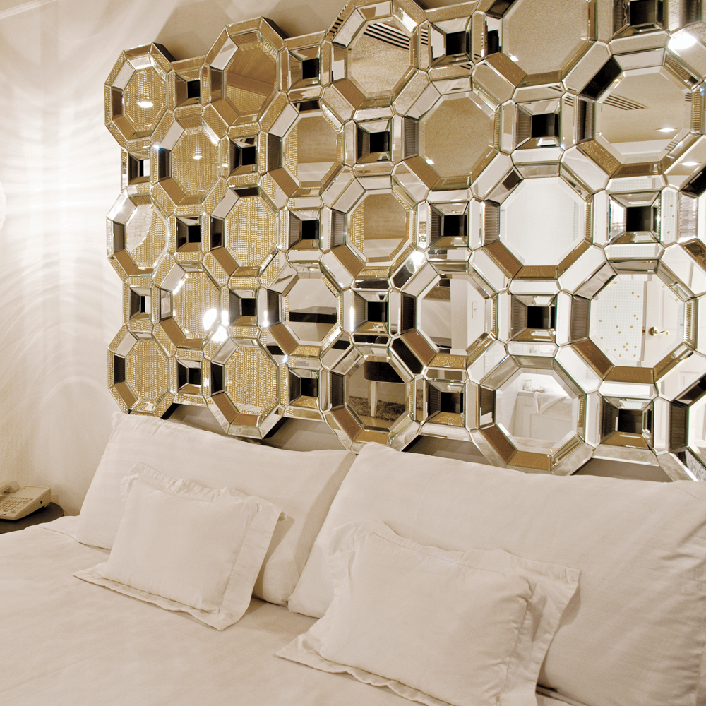 The geometric Crawford Wall Mirror serves as a headboard in a clean, white bedroom