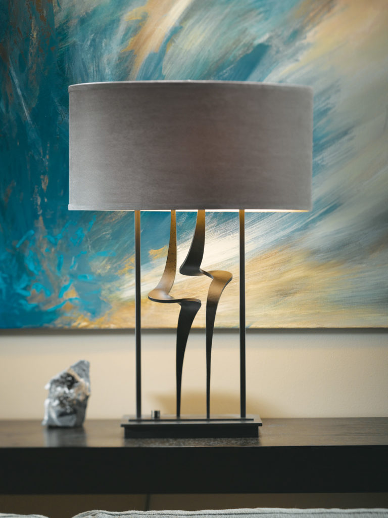 Antasia table lamp has two hand-forged lightning bolt swivels that mirror modern artwork behind it.