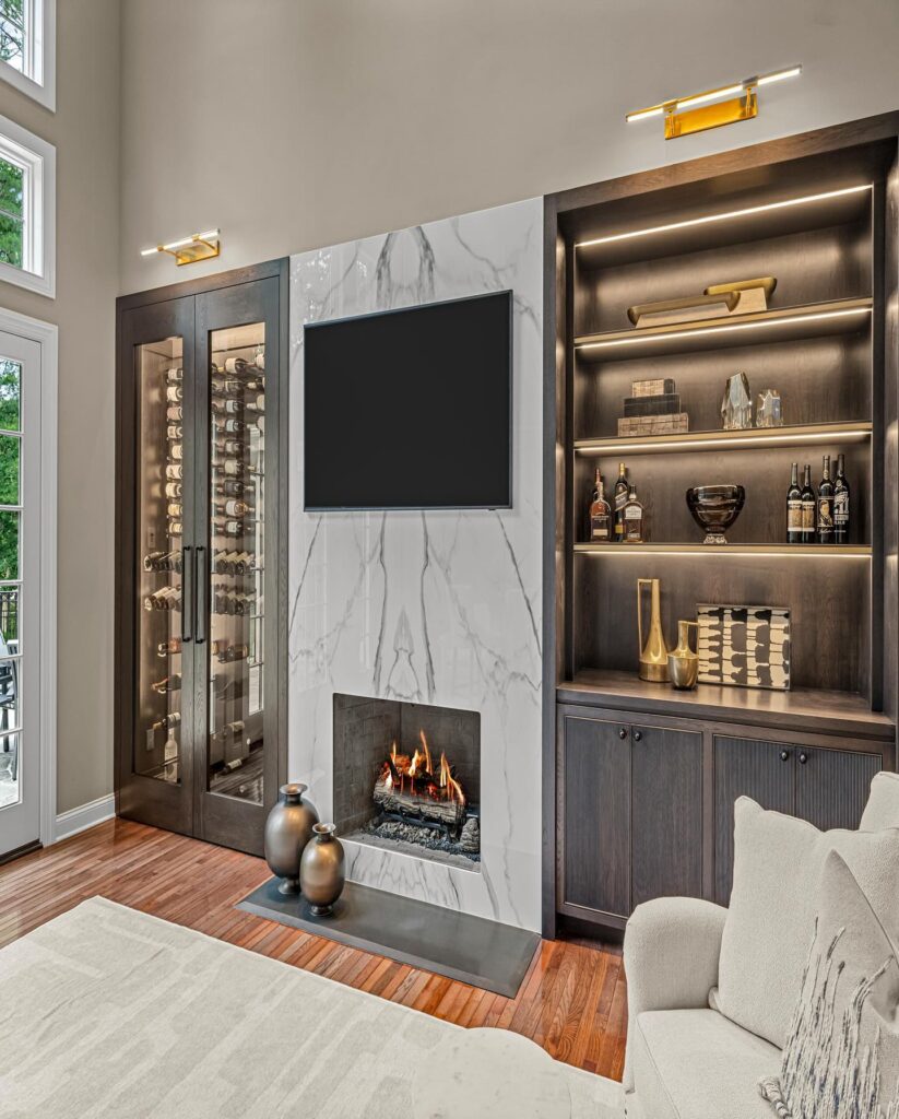 Living room with built-in accent lighting, featuring a marble fireplace with a TV above, a glass wine cabinet on the left, and illuminated shelving with decorative items.