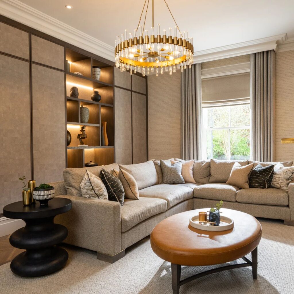 Cozy modern living room with a beige sectional, built-in accent lighting, and a crystal chandelier.