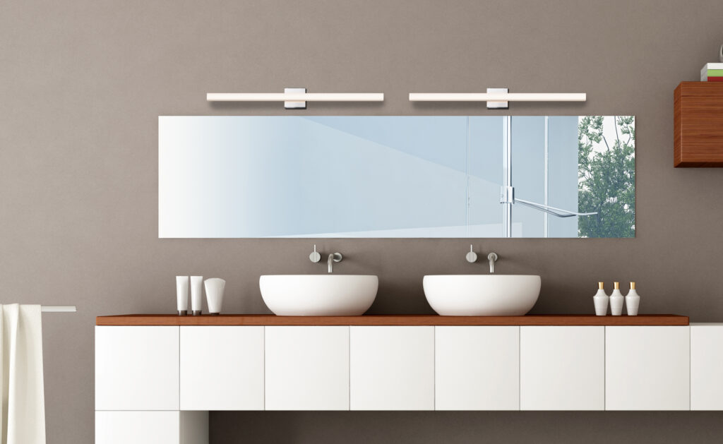 A contemporary bathroom with a mirror illuminated by a Sonneman Bathroom Vanity Light, above a white sink with a wooden cabinet.