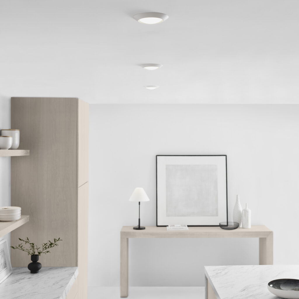 A minimalist room with three circular recessed lights on a white ceiling, a wooden console table, and a framed picture.