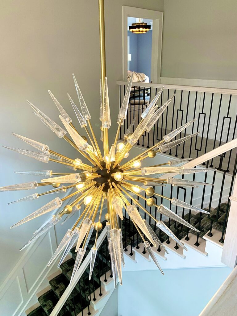 Gold Sputnik chandelier with glass spikes hanging above a modern staircase with black railings.