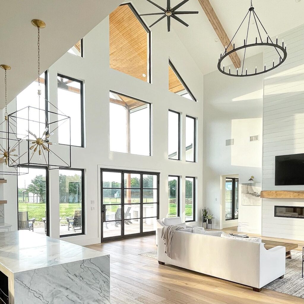 Open-concept living room with a high vaulted ceiling, large windows, and modern decor.