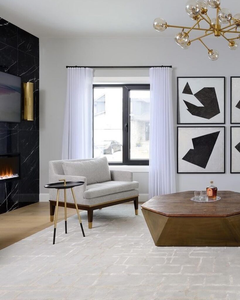A chic living room with a black marble fireplace, a light grey armchair, a modern coffee table, and abstract art prints.