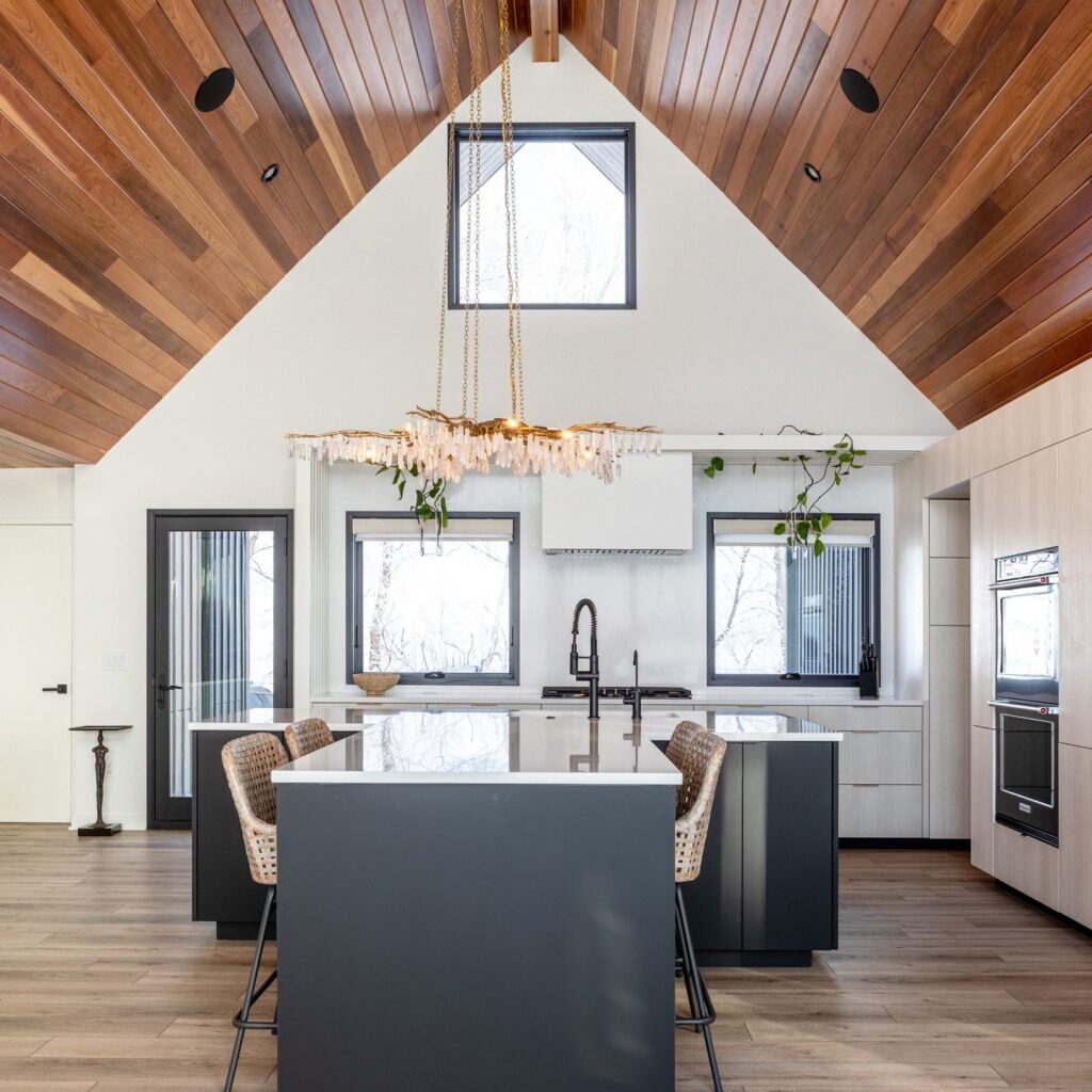 Modern kitchen with vaulted wood ceiling, dark island, and a large chandelier.