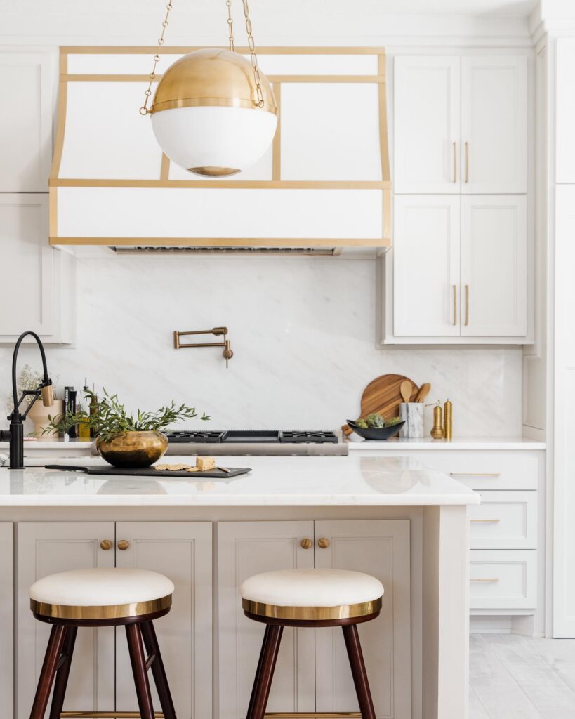 Bright kitchen with gold accents, white cabinetry, marble backsplash, and modern globe pendant.