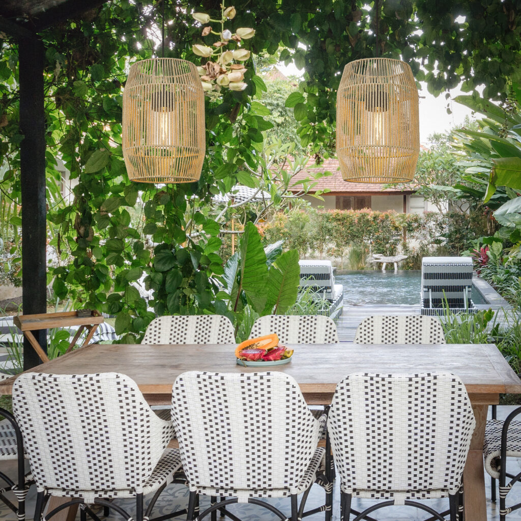 Pergola dining area with woven pendant lights over a garden table by the pool.