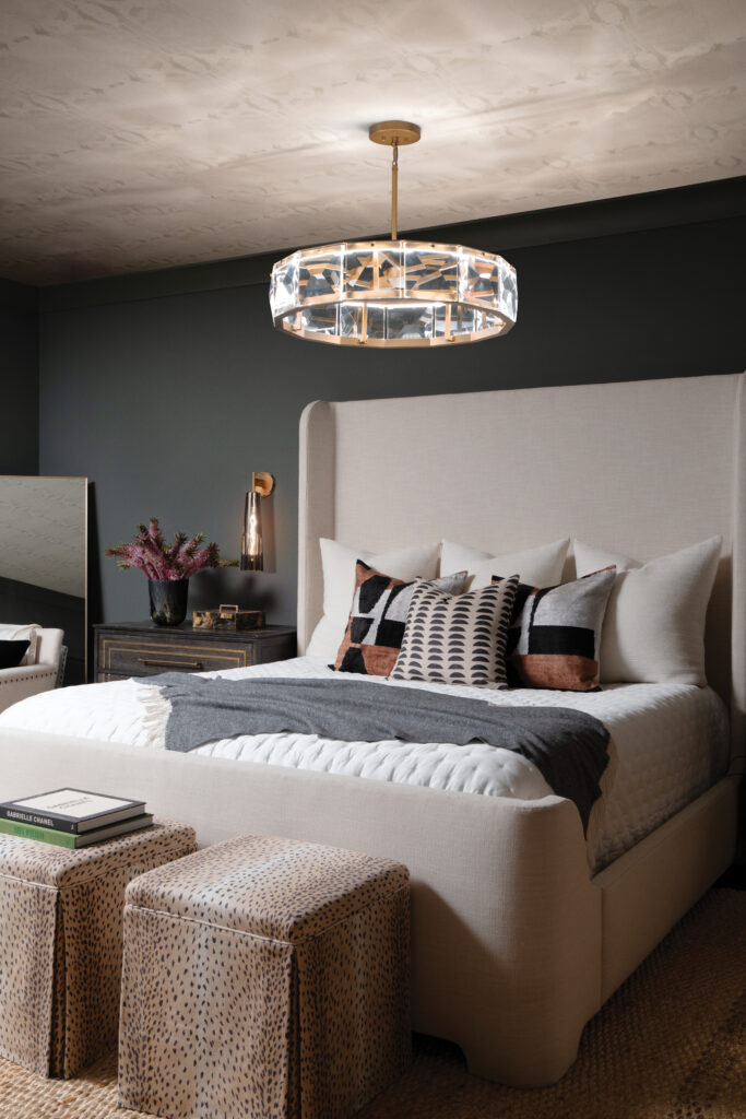 Bedroom with crystal chandelier and brass wall sconce beside upholstered bed.